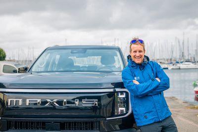 Conrad Colman est en tenu de voile adossé à un pick up électrique de la marque MAXUS devant le port de plaisance